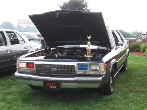 1991 Ford LTD Crown Victoria - black-and-white Ford sedan sits with its hood up at a show, a trophy on the engine and a DARE plate on the front bumper.