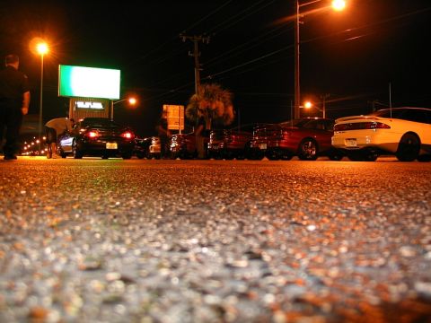 1997 Ford Probe - A group of cars are parked side-by-side on a street at night, illuminated by streetlights and a large billboard.