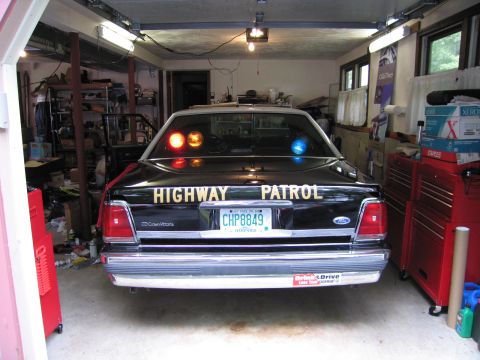 1991 Ford LTD Crown Victoria - Rear view of a black Ford LTD Crown Victoria lettered Highway Patrol with red and blue lights lit, parked in a garage.