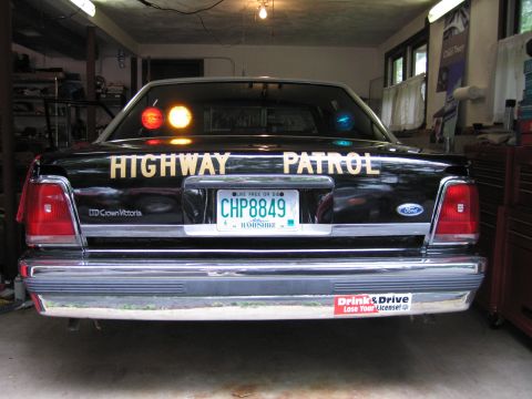 1991 Ford LTD Crown Victoria - Rear of a black Ford LTD Crown Victoria lettered Highway Patrol, plate CHP8849, with a Drink and Drive bumper sticker, in a garage.