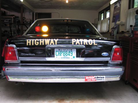 1991 Ford LTD Crown Victoria - Rear of a black Ford LTD Crown Victoria lettered Highway Patrol with NH plate CHP8849 and amber light lit, inside a garage.