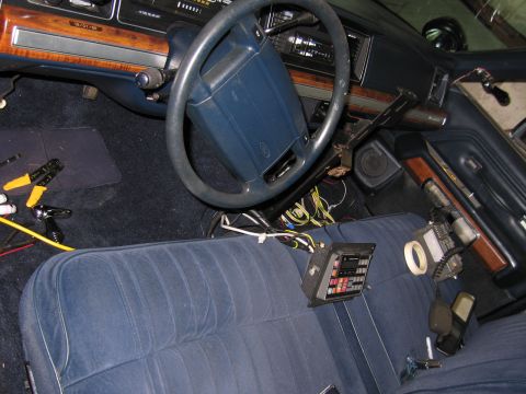 1991 Ford LTD Crown Victoria - Front interior of a Ford sedan showing a blue cloth bench seat, woodgrain dash, steering wheel, and a mounted electronic control box.