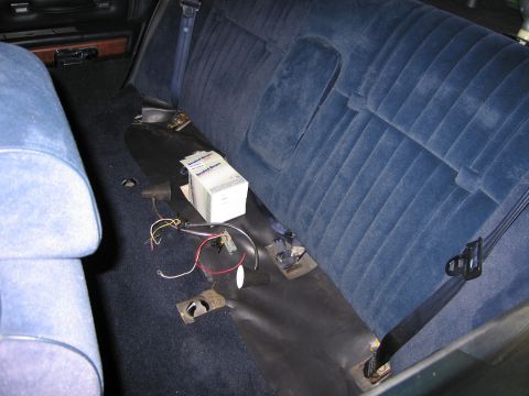 1991 Ford LTD Crown Victoria - blue rear bench area of a sedan with the seat lifted, exposing floor wiring, mounting brackets, and a small white box.