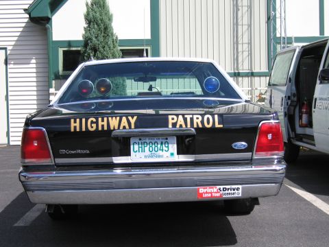 1991 Ford LTD Crown Victoria - Rear of a black Ford LTD Crown Victoria lettered Highway Patrol with NH plate CHP8849, parked outdoors beside a van.