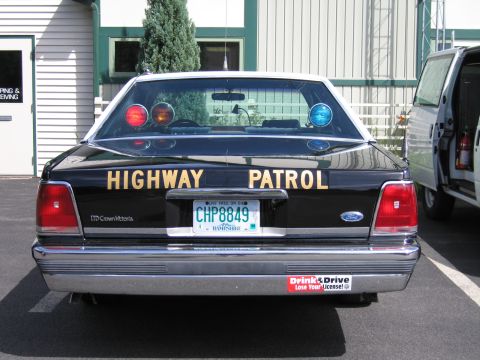 1991 Ford LTD Crown Victoria - Rear of a black Ford LTD Crown Victoria lettered Highway Patrol, plate CHP8849, with red and blue deck lights, parked outdoors.