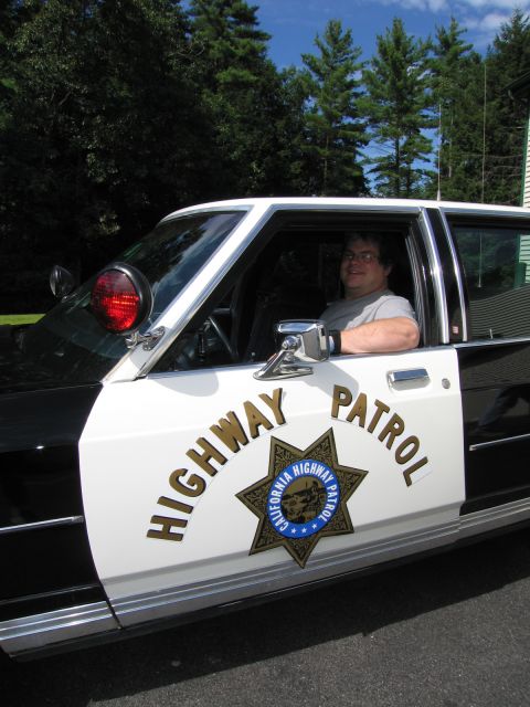 1991 Ford LTD Crown Victoria - Close-up of a black-and-white sedan's front door bearing the gold California Highway Patrol star emblem, a man visible in the driver seat.
