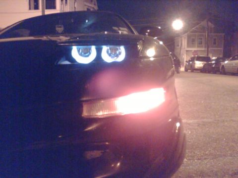 1997 Ford Probe - A black car is seen at night with its distinctive halo headlights illuminated, alongside other vehicles parked on a street.
