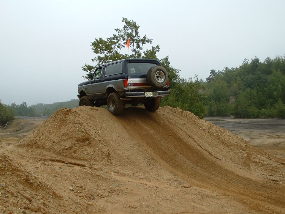 1995 Ford Bronco climbing a dirt mound with an orange flag on its antenna