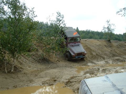 1995 Ford Bronco - A red Jeep tackles a challenging muddy terrain, with the front of another vehicle visible in the foreground.