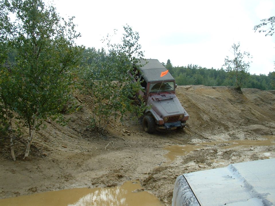 Red Jeep navigating a muddy off-road course, with another vehicle visible in the foreground