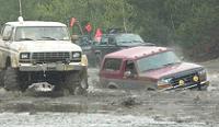 1995 Ford Bronco - Multiple off-road vehicles navigate a muddy terrain, with one red SUV partially submerged.