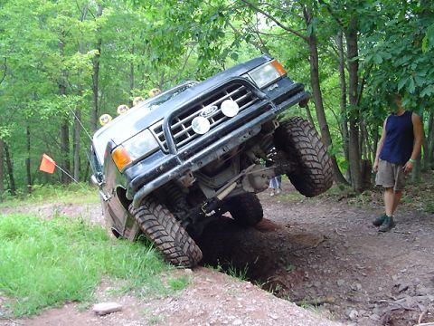 1979 Ford Bronco - This black SUV is tilted precariously on a dirt trail, with its front grille and off-road tires clearly visible.
