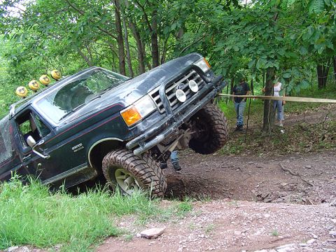 1979 Ford Bronco - Modified SUV tackling challenging off-road terrain with one wheel elevated.