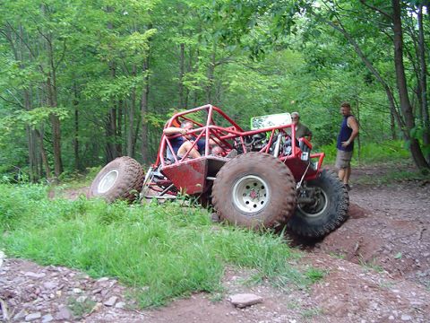 1979 Ford Bronco - A custom-built off-road buggy with a roll cage is shown traversing a challenging dirt path in a wooded area.