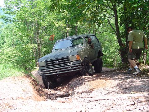 1979 Ford Bronco - A green Ford Bronco navigates a challenging off-road trail with a driver visible inside.
