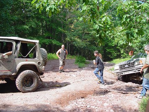 1979 Ford Bronco - Two off-road vehicles are stuck in the mud on a wooded trail, with people attempting to free them.