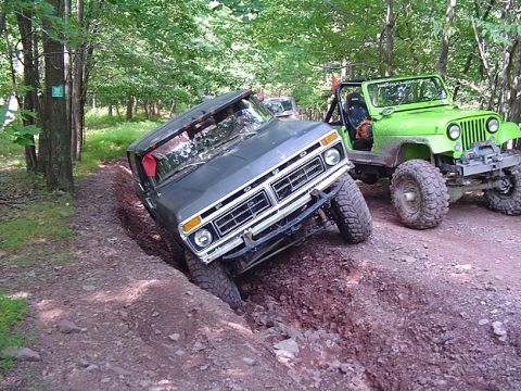 1979 Ford Bronco - Two off-road vehicles navigate a challenging dirt trail with one vehicle stuck in a deep rut.
