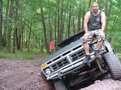 1979 Ford Bronco - A man sits atop the grille of a gray 1979 Ford Bronco as it navigates an off-road trail.