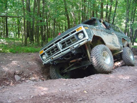 1979 Ford Bronco - A modified 1978 Ford Bronco navigates a challenging off-road trail in a wooded area.