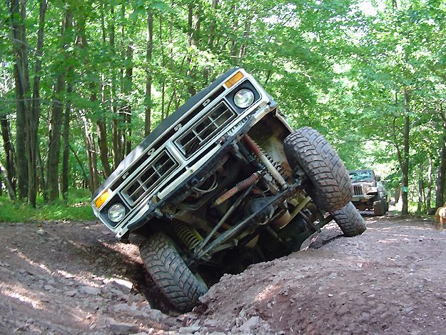 Ford Bronco tilted on its side on a muddy trail with another Jeep in the background