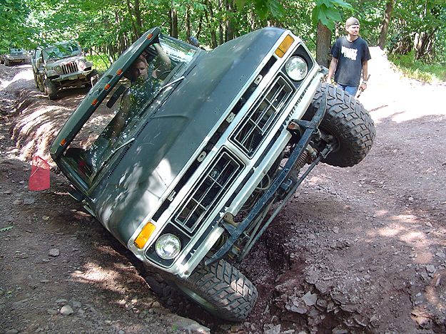 Dark green 1978 Ford Bronco tilted in a ditch off-road, with a man standing nearby