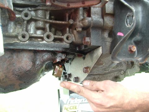 1996 Ford Probe - Close-up view of a damaged engine oil pan, indicating a leak. A finger points to the affected spot.