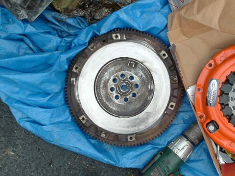1996 Ford Probe - A clutch disc and flywheel assembly are laid out on a blue tarp, with a drill visible in the foreground.