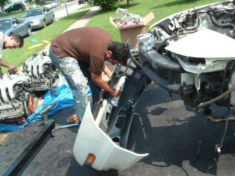 1996 Ford Probe - Car engine and bumper assembly being worked on by two people, with another vehicle in the background.