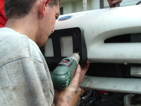 1996 Ford Probe - A person is using a drill to work on the front grille of a white vehicle.