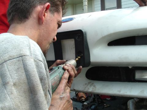 1996 Ford Probe - A man drills a hole in the front bumper of a white 1996 Ford Probe.