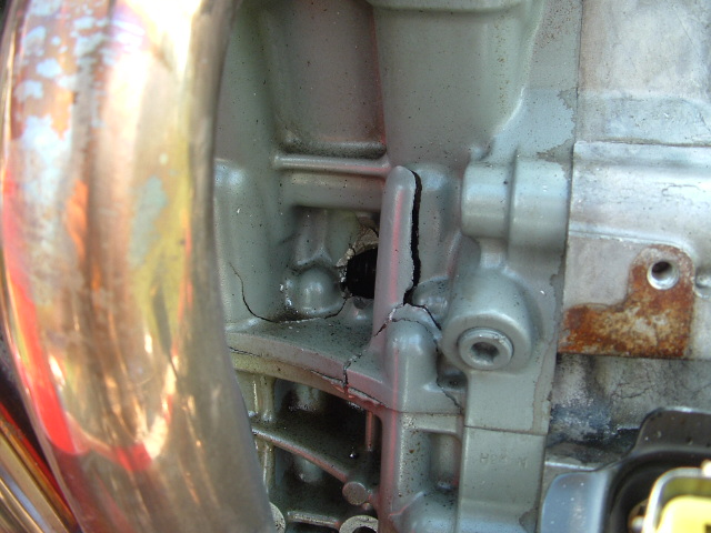 Engine block with large cracks and a hole, showing metallic texture and some rust
