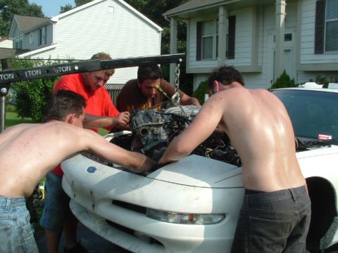 1996 Ford Probe - Four men work together to remove the engine from a white Ford Probe using an engine hoist.