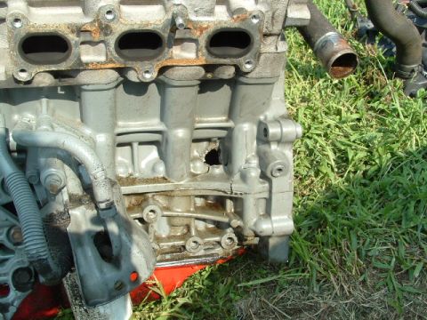 1996 Ford Probe - Engine block with a hole and crack in the casing, sitting on grass.