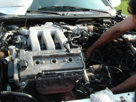 1996 Ford Probe - Hands working on a car's engine bay, with "MAZDA" visible on the intake manifold.