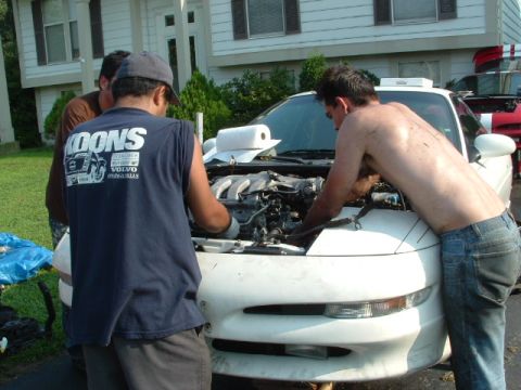 1996 Ford Probe - Two men are actively working on the engine of a white Ford Probe, with another person observing.