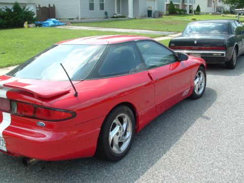 1996 Ford Probe - A red 1996 Ford Probe with distinctive white racing stripes is parked on a residential street.