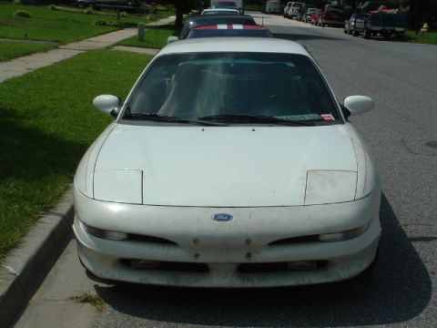 1996 Ford Probe - A white 1996 Ford Probe is parked on the side of a residential street, with other vehicles lined up behind it.