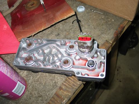 1995 Ford Bronco - A transmission solenoid body with a red and green electrical connector sits on a workbench next to a can of spray.