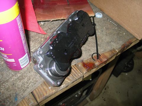 1995 Ford Bronco - A mechanical part, possibly a solenoid, sits on a wooden workbench next to a purple spray can and a bottle cap.