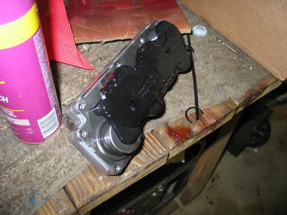 Black and metal auto part with shaft on a workbench near a spray can