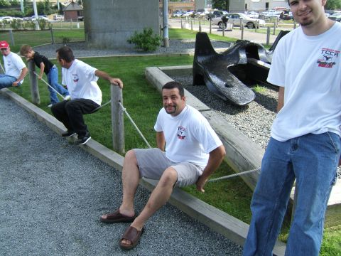 1998 Ford Taurus - Several men relax on a wooden beam in an outdoor setting, with a large, dark metal sculpture in the background.