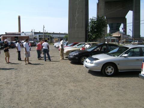 1998 Ford Taurus - A silver 1998 Ford Taurus is parked in a lot with other vehicles under a large bridge structure.