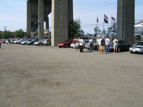 1998 Ford Taurus - A gathering of people and vehicles in a parking lot beneath a bridge.