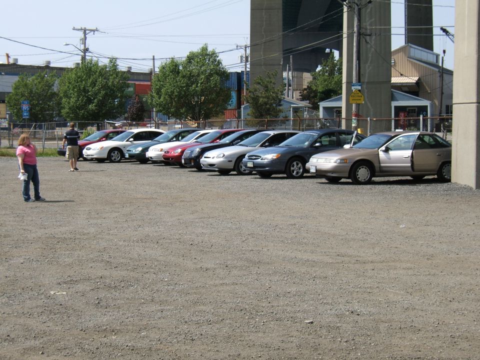 row of cars parked on gravel lot, one car has door open