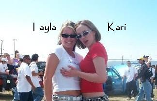 2005 BMW 3 Series - Layla and Kari pose for a photo at an outdoor event with a crowd and a blue car visible.
