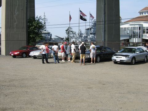 1998 Ford Taurus - Several cars are parked in a lot near a waterfront, with large ships visible in the background.