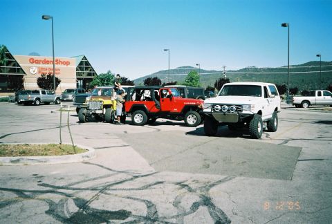 1990 Ford Bronco - small Jeep, red Wrangler and white lifted SUV gather in a parking lot near a Garden Shop store, dated August 2005.
