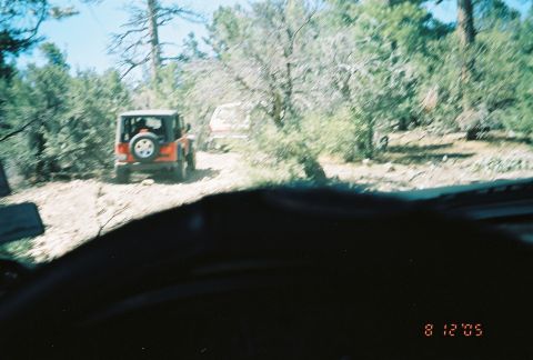 1990 Ford Bronco - red open Jeep and a white vehicle travel a wooded dirt trail, viewed over a dark dashboard, dated August 2005.