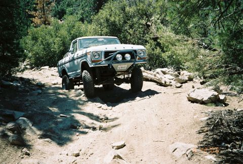 1990 Ford Bronco - lifted older pickup with auxiliary lights on its brush guard works down a rocky forest trail.