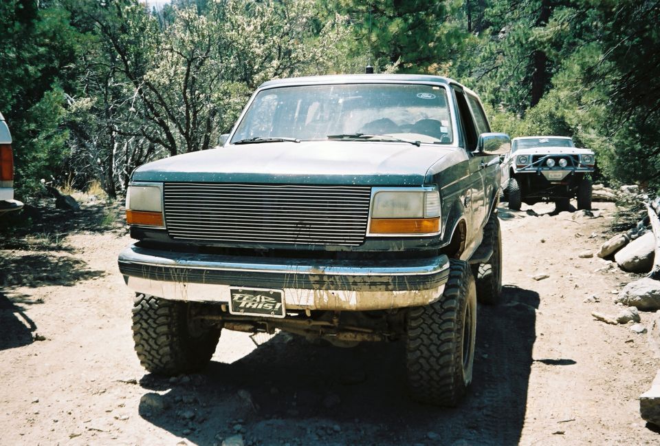 Lifted Ford full-size SUV with billet grille on a dirt trail, second truck behind